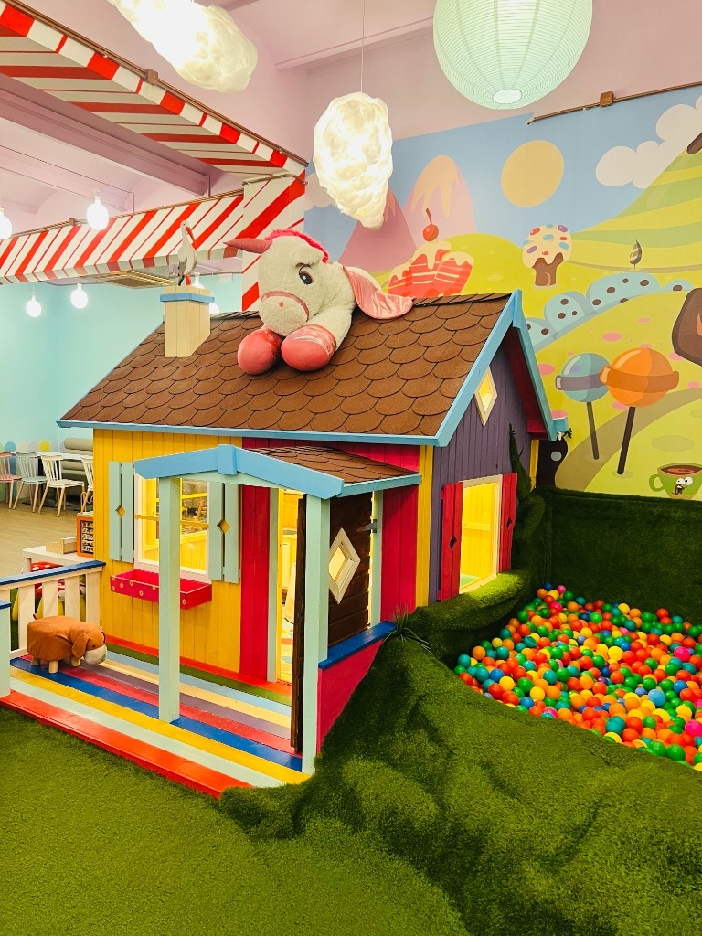 Casita de juegos amarilla de Charlie Restaurante, con unicornio en el tejado y zona de juego al lado