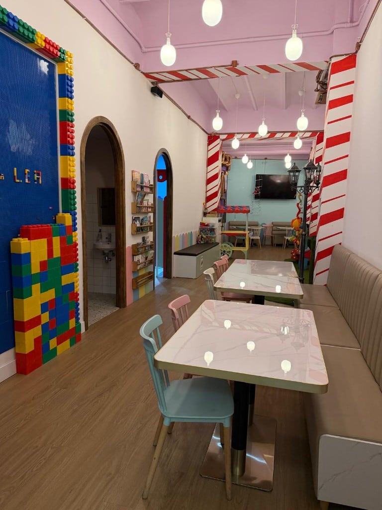 Pasillo del comedor de Charlie, con mesas, pared de construcciones y carrito de juguete
