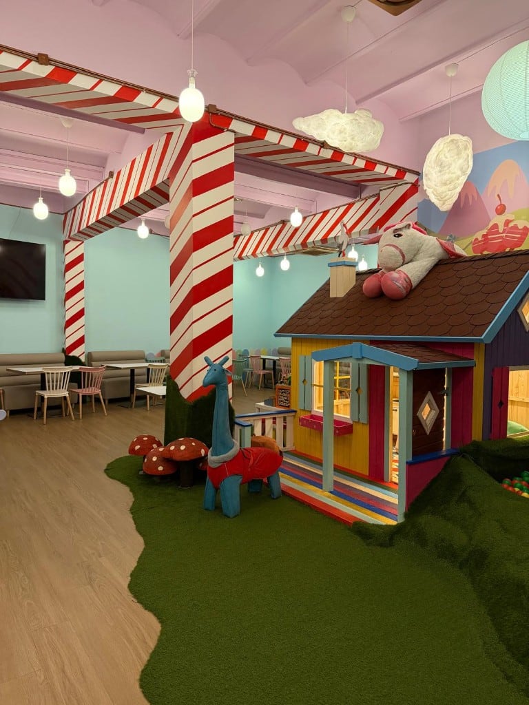 Salón de Charlie con casita de juegos, piscina de bolas, columnas de caramelo y comedor al fondo