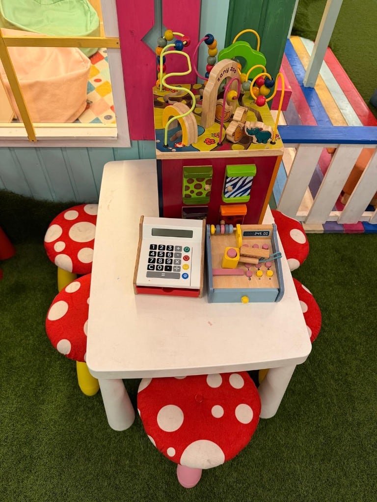 Mesa infantil con taburetes de seta y juguetes de madera en la zona de juegos de Charlie